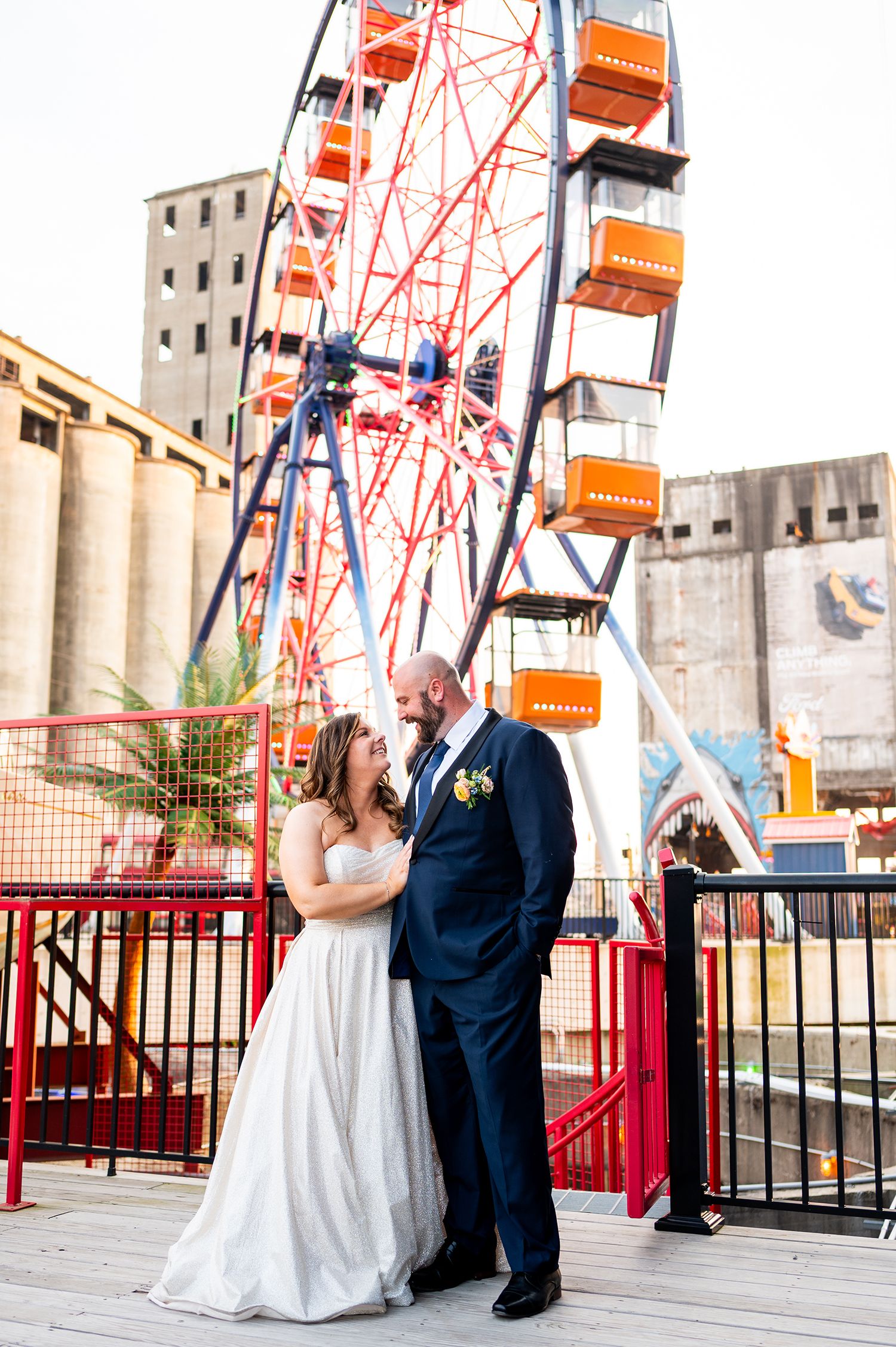 Newlyweds posing for photos in front of a red Ferris wheel at an amusement park.