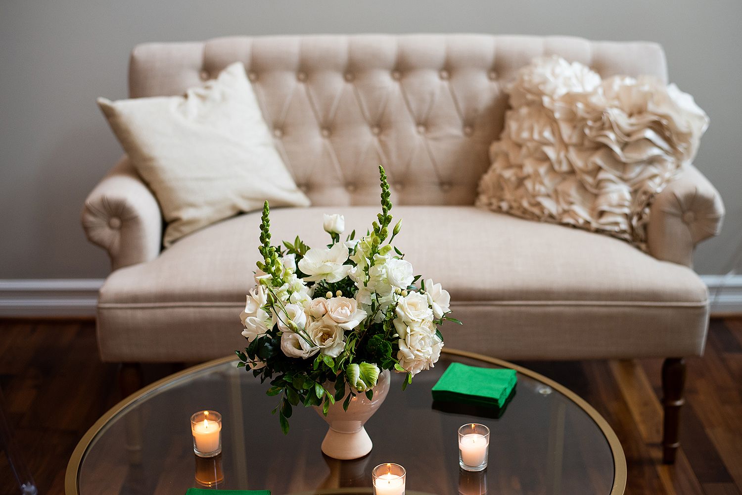 Elegant tufted beige sofa with decorative pillows and floral centerpiece on round coffee table with lit candles.