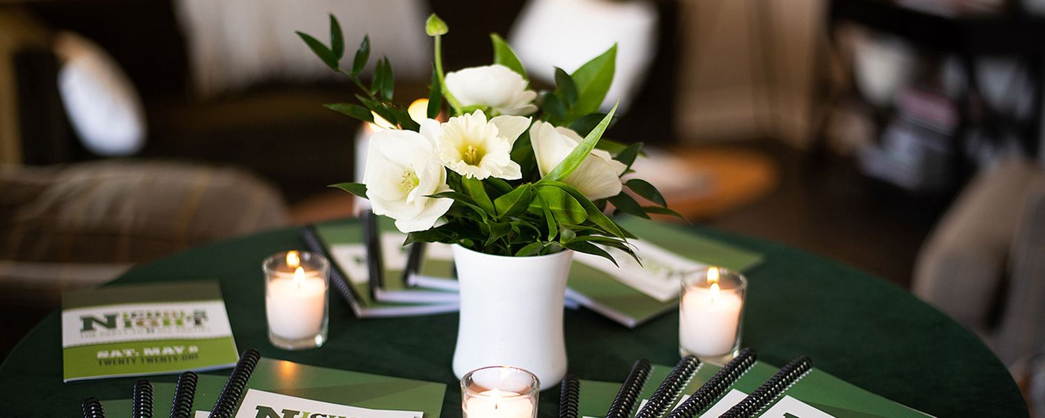 Elegant wedding reception tables decorated with white floral centerpieces, candles, and lush greenery create an intimate atmosphere.