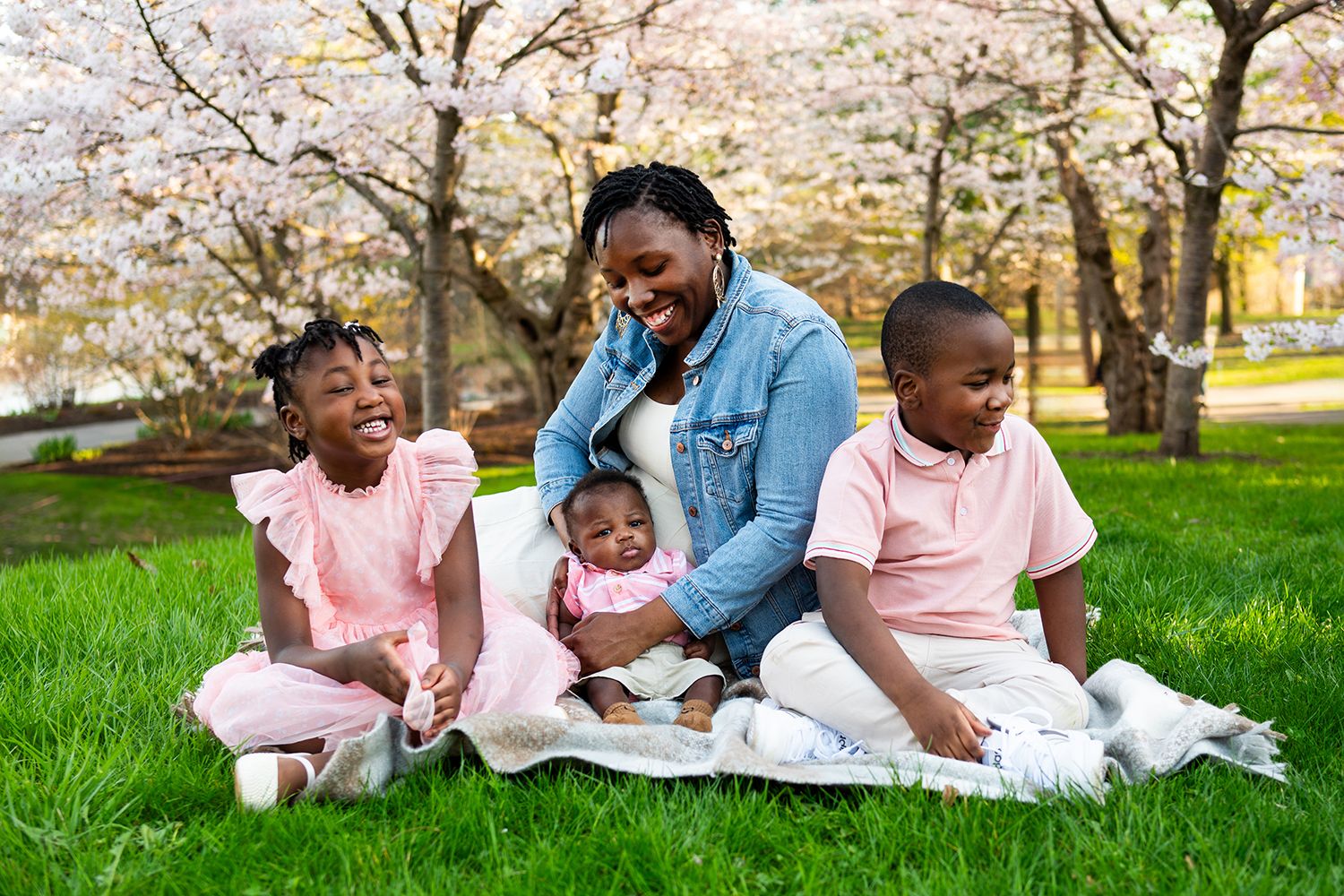 Family enjoying springtime together during outdoor photoshoot beneath pink cherry blossoms.