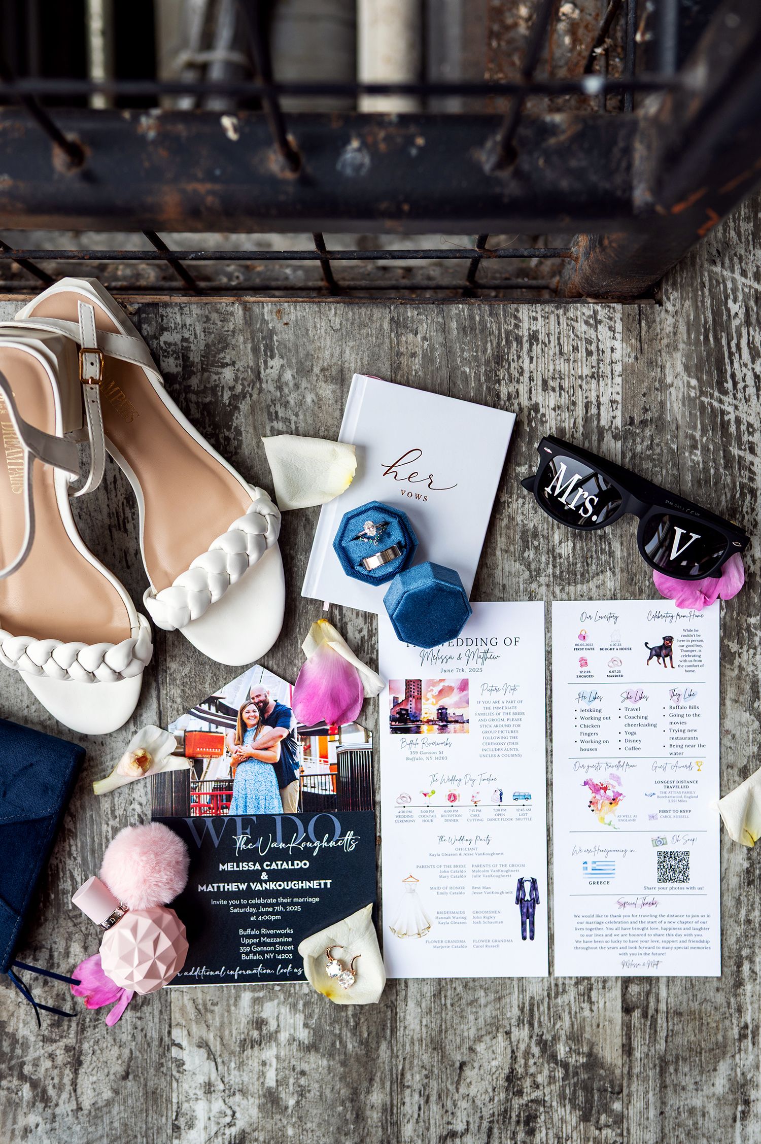Wedding invitation suite with pink and blue accents displayed on rustic wooden background with scattered floral elements.