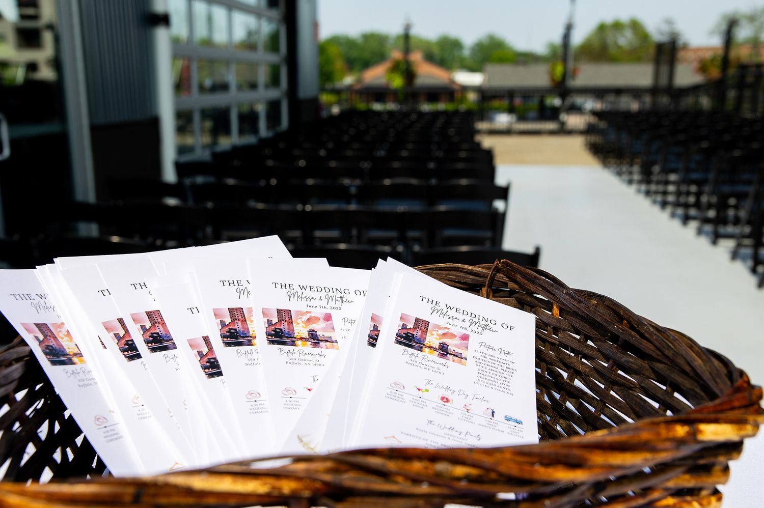 A row of black folding chairs arranged outdoors for an event with printed programs on each seat.