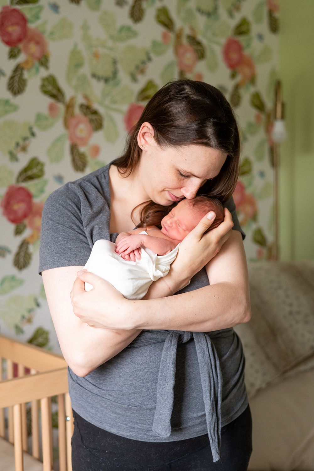 A tender moment between parent and newborn against a floral wallpaper background in a nursery.
