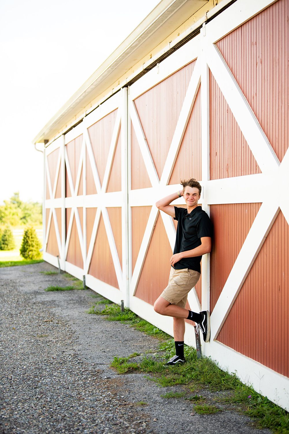 Casual portrait against coral-colored barn wall with white trim and geometric patterns.