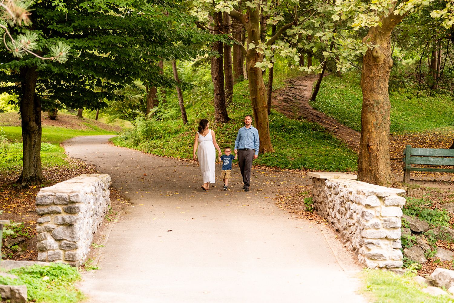 A couple walks together on a peaceful winding path through a lush green park with stone walls bordering the trail.