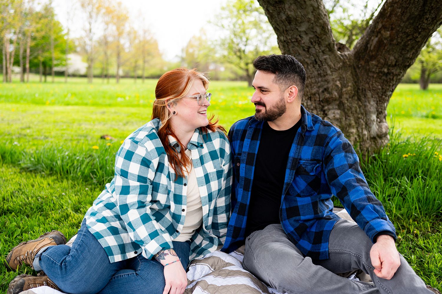 Couple relaxing on blanket under blooming tree branches in lush spring grass.