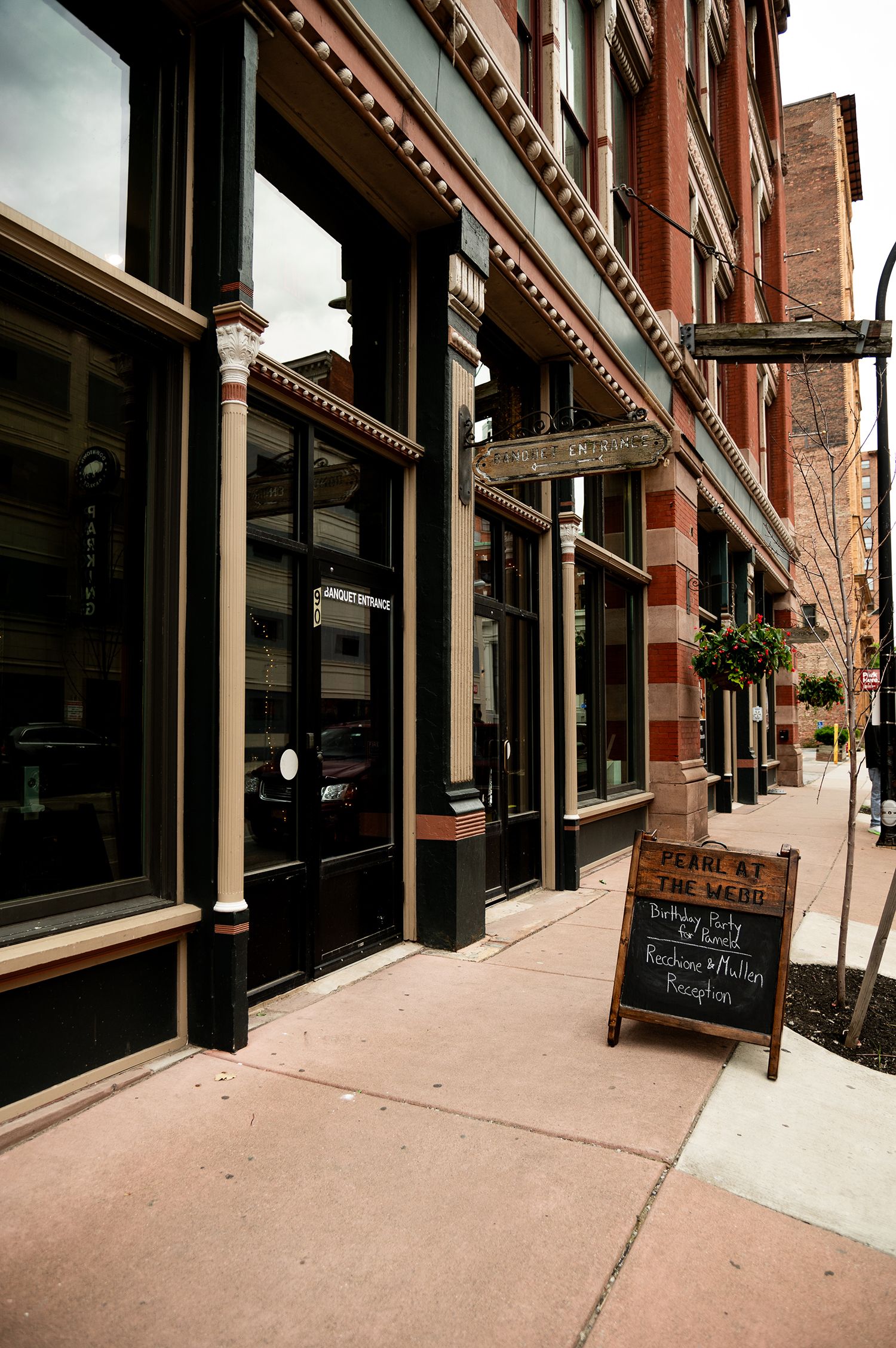 Historic brick building storefront with chalkboard sandwich sign on urban sidewalk.