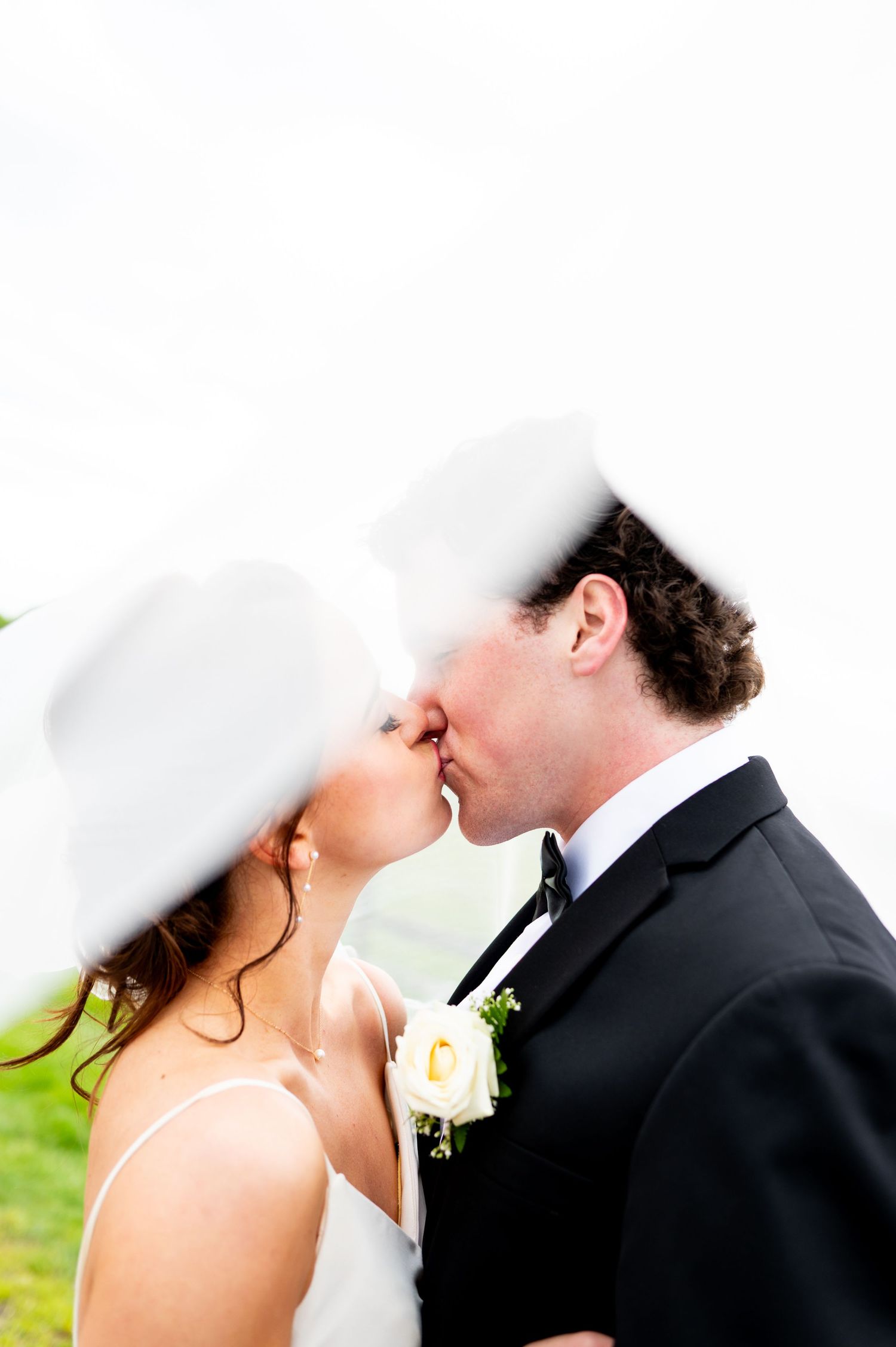 A romantic wedding couple shares an intimate kiss outdoors with greenery in the background.
