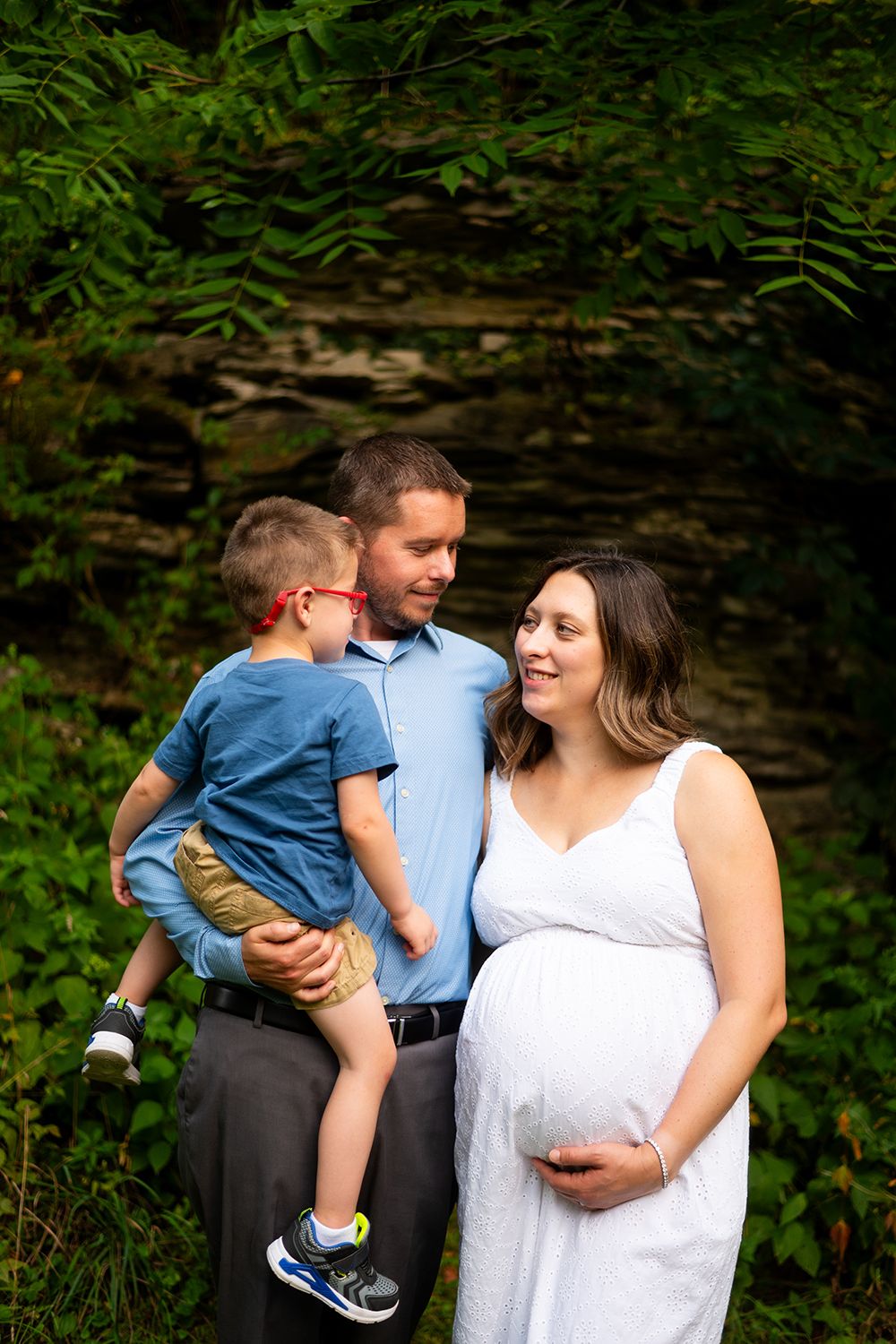 A family shares a joyful moment outdoors as they await their new arrival, with lush greenery in the background.