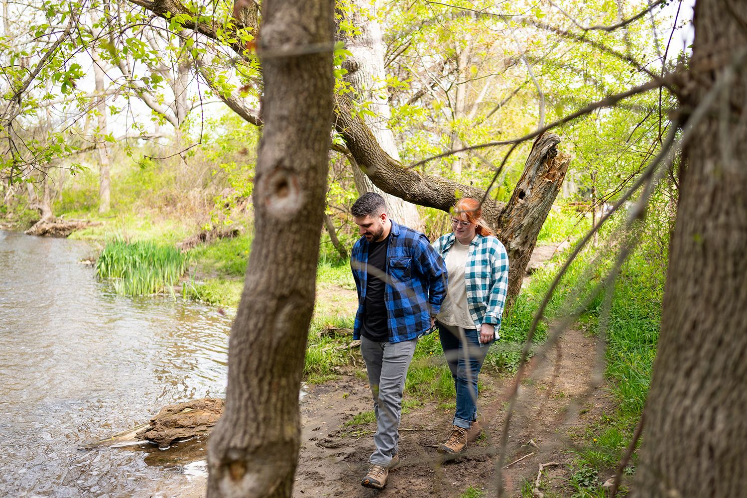 Two people walking on a dirt path along a creek surrounded by spring trees with fresh green foliage.