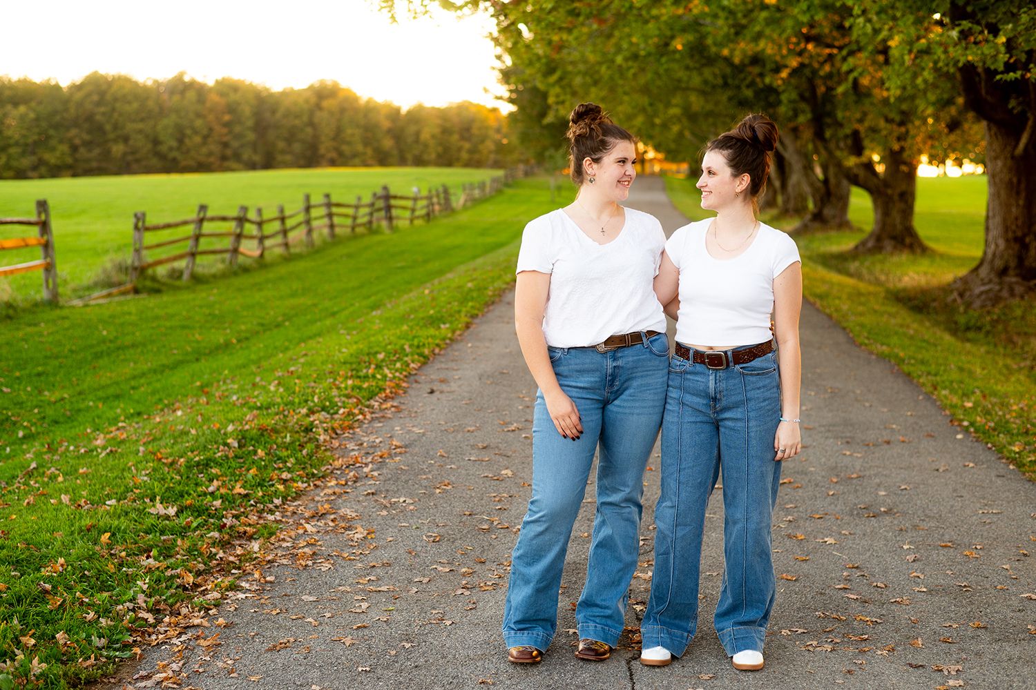 Two people walking together down a peaceful country path lined with fall foliage and wooden fencing.