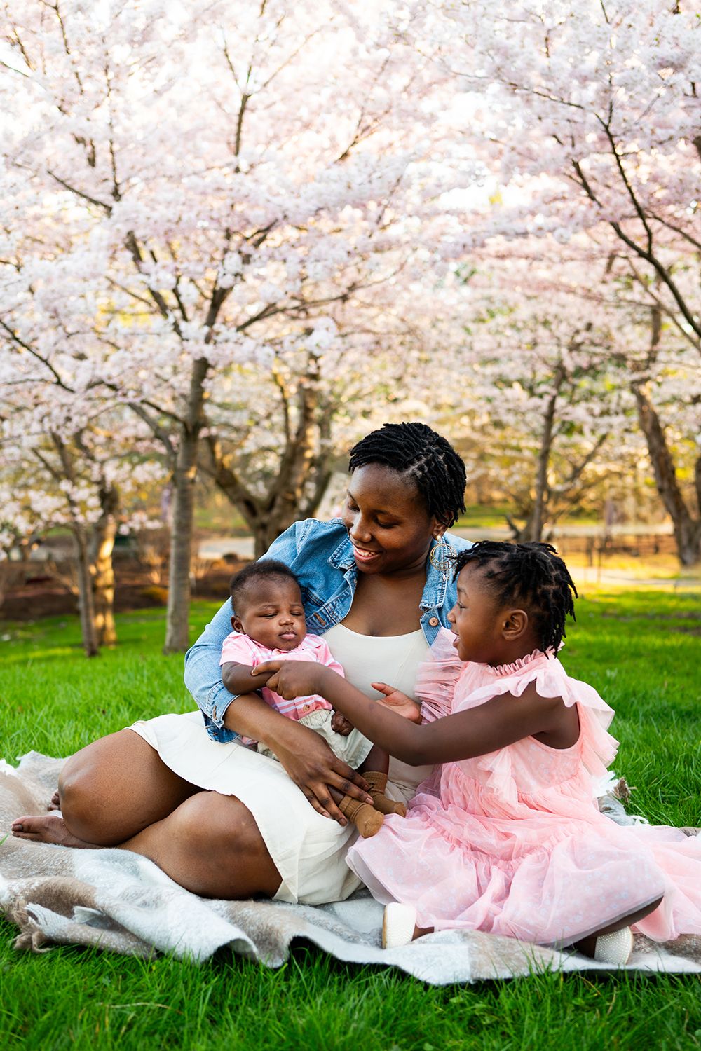 A family shares a tender moment while sitting on a blanket under blooming cherry blossom trees in spring.