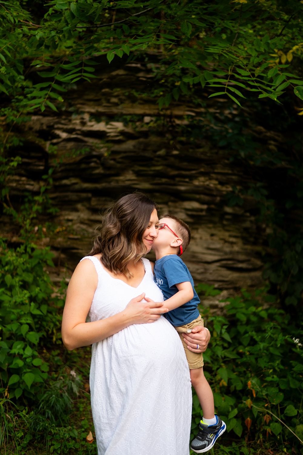 A tender moment captured against a stone wall backdrop surrounded by lush green foliage.