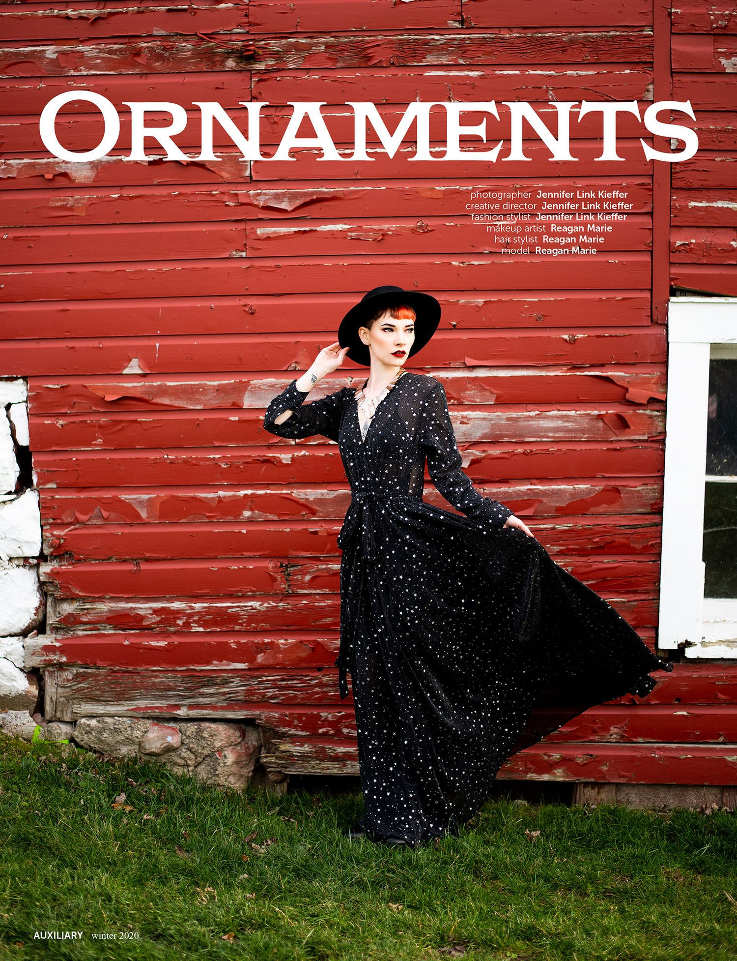 A long black velvet dress against a rustic red barn with white trim and the word 'Ornaments' painted above.