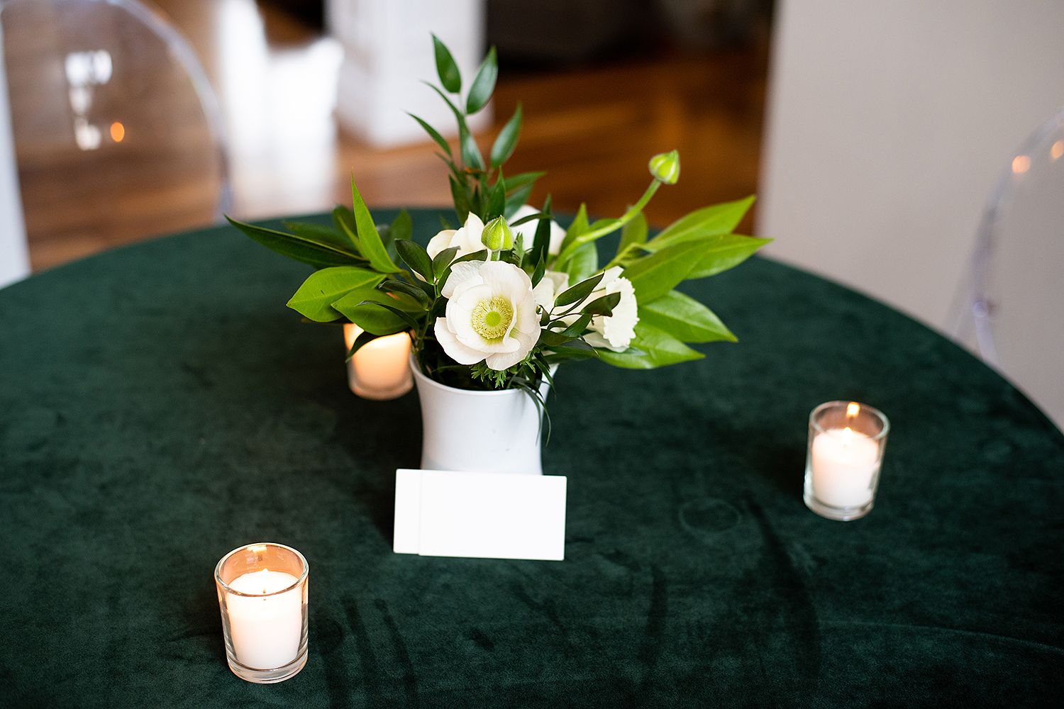 White floral centerpiece in a white vase with lit candles on a dark green velvet tablecloth.