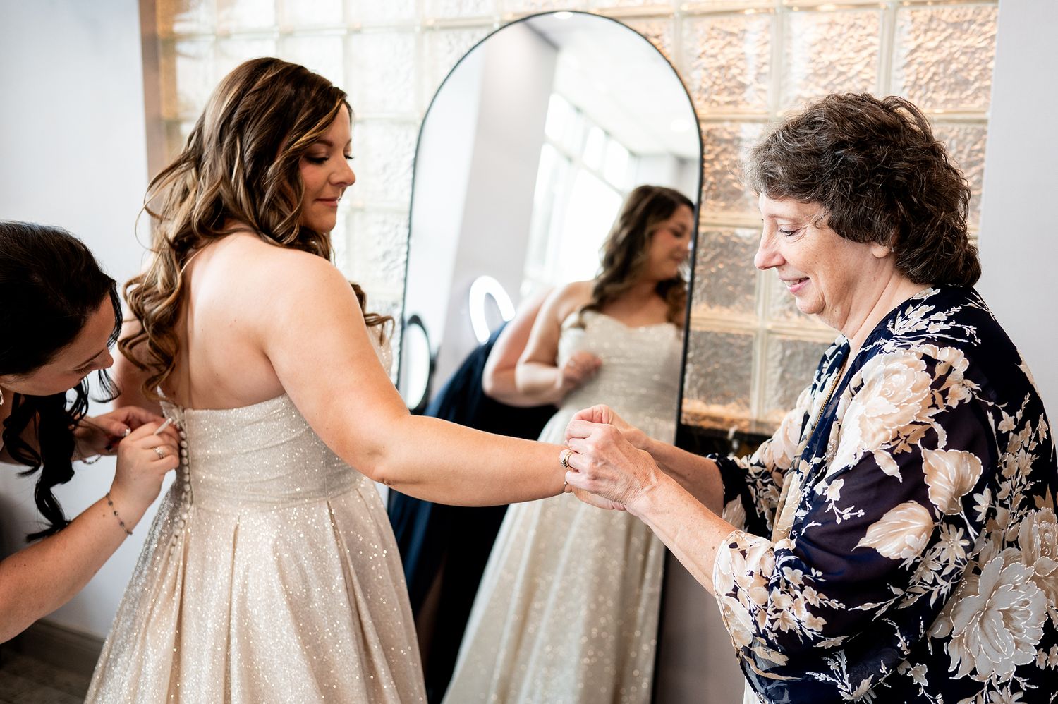 Wedding party helping with final dress preparations in a rustic brick interior.