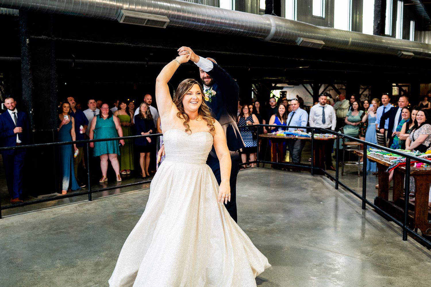 A person in a flowing white wedding dress dances joyfully at a reception venue while guests look on from the sidelines.