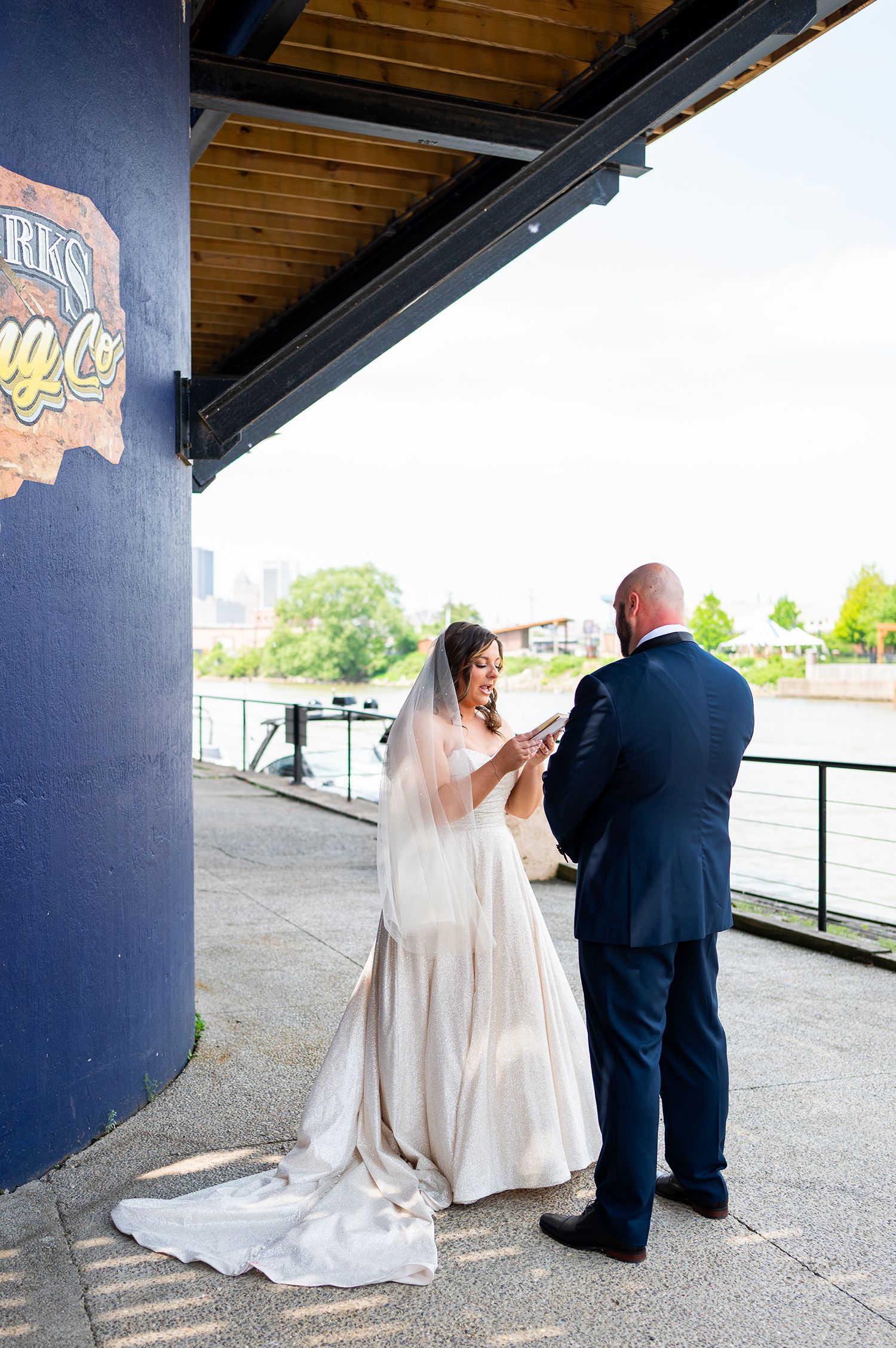 A couple shares an emotional moment during their wedding ceremony on a covered outdoor deck by the water.