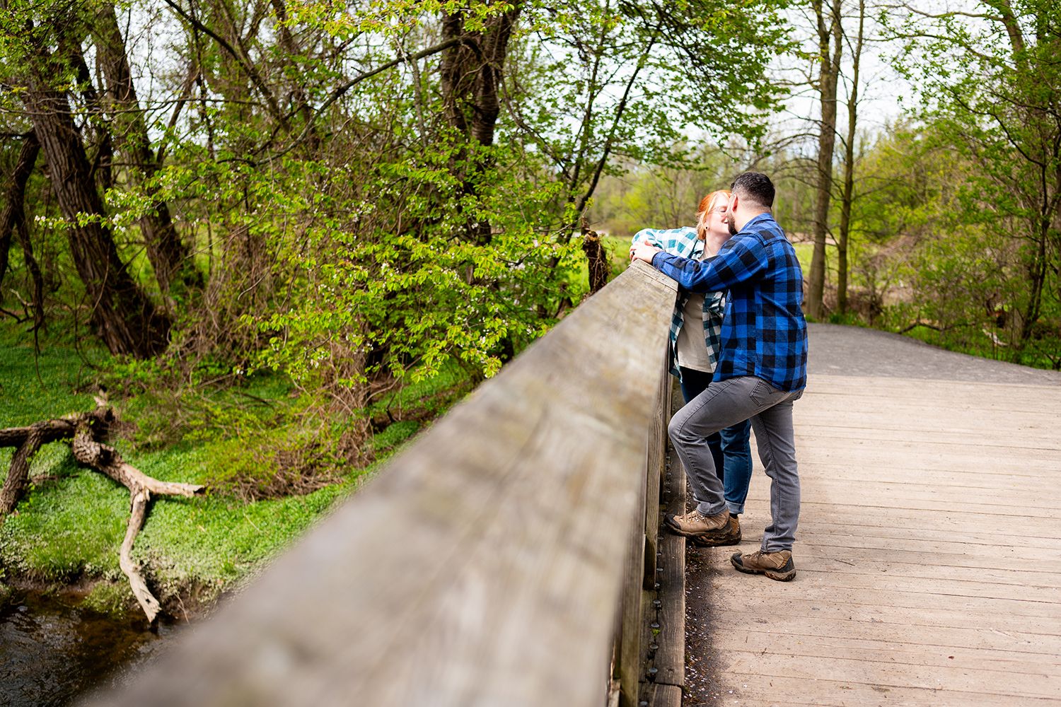 A couple walks hand in hand along a scenic woodland pathway surrounded by lush spring greenery and trees.