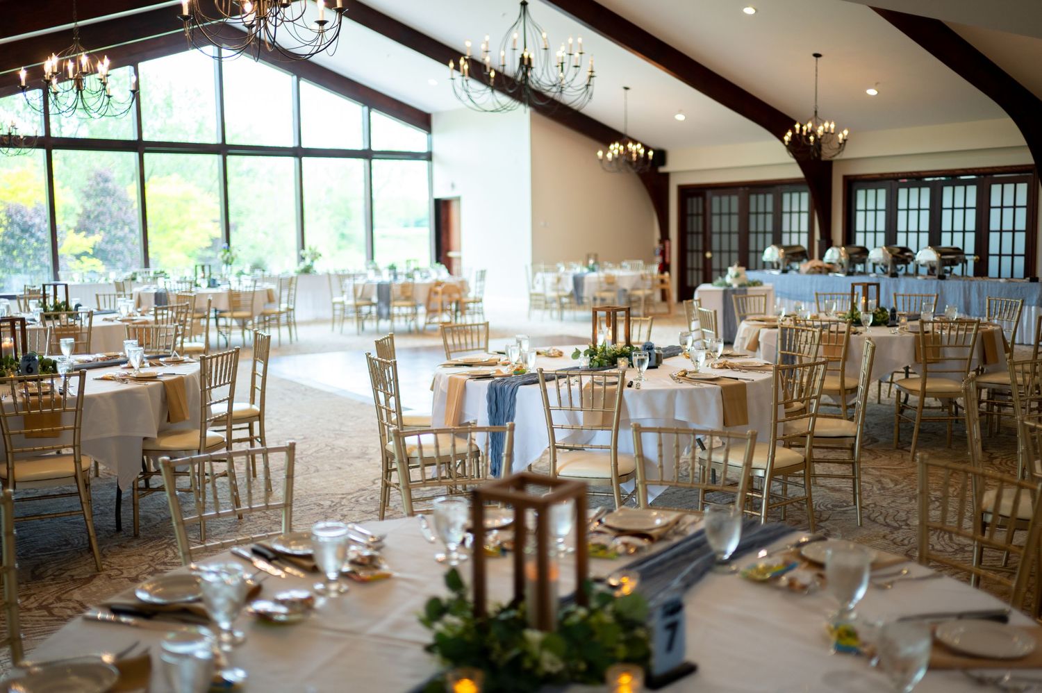 Elegant wedding reception venue with white tablecloths, chiavari chairs and large windows overlooking a scenic view.