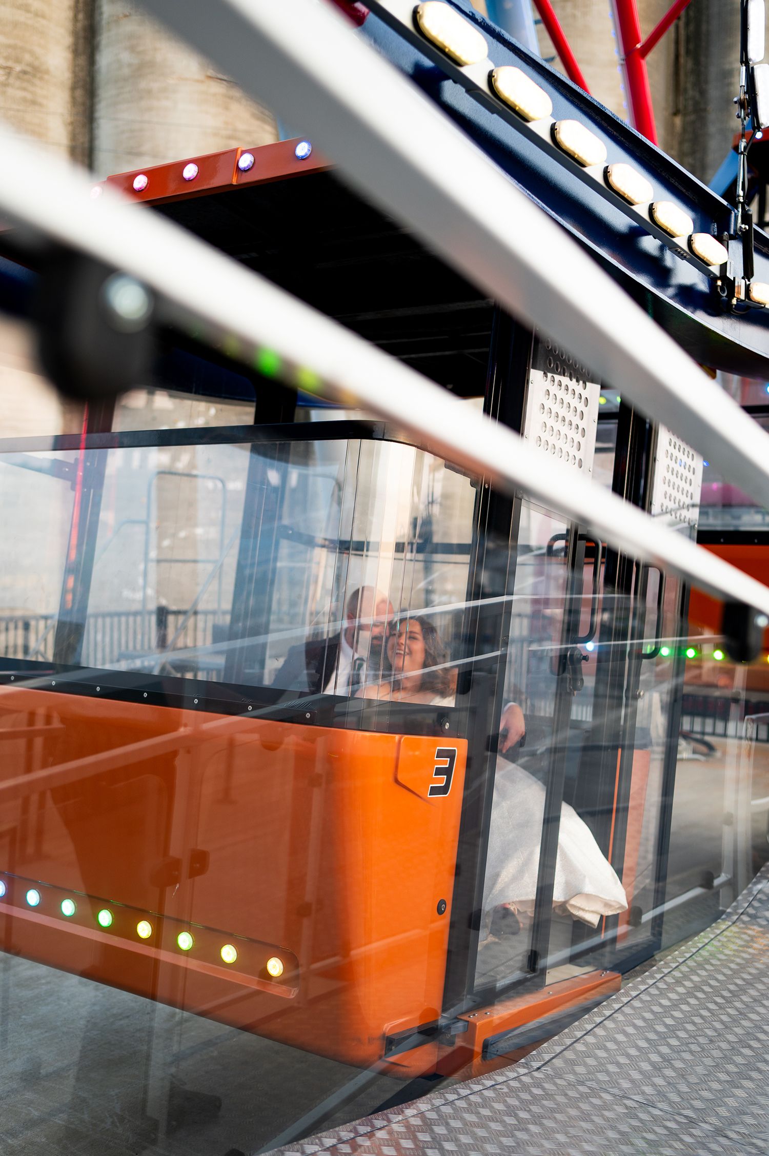 Orange glass panels with white dots line a modern building entrance with metal framing and reflective surfaces.