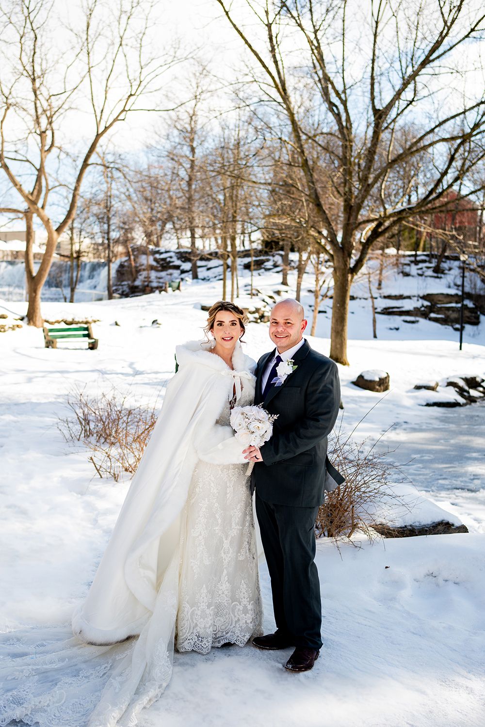 A winter wedding portrait featuring a lace gown and white cape against a snowy landscape.