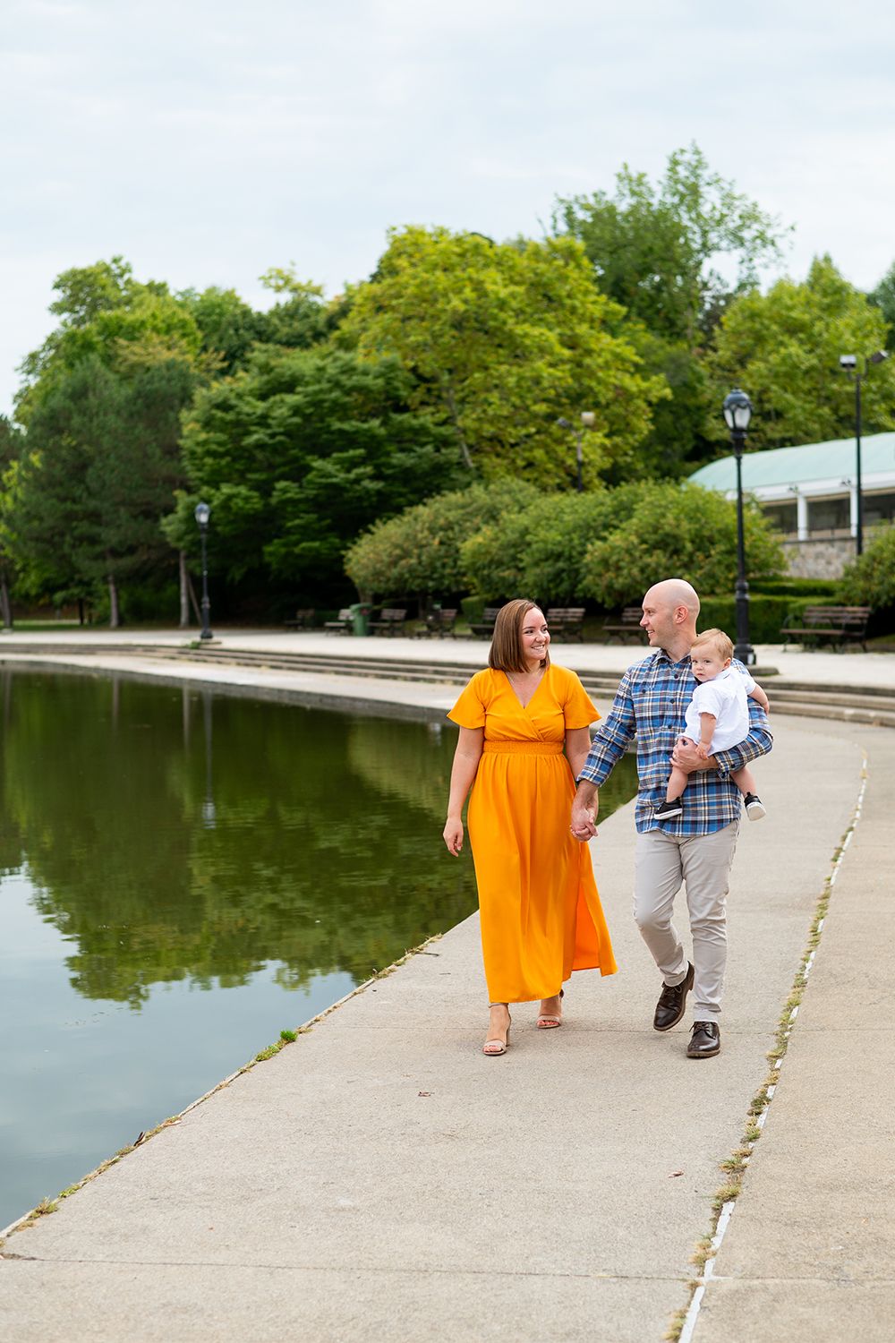 A couple walks together along a waterfront path next to a serene pond on a sunny summer day.