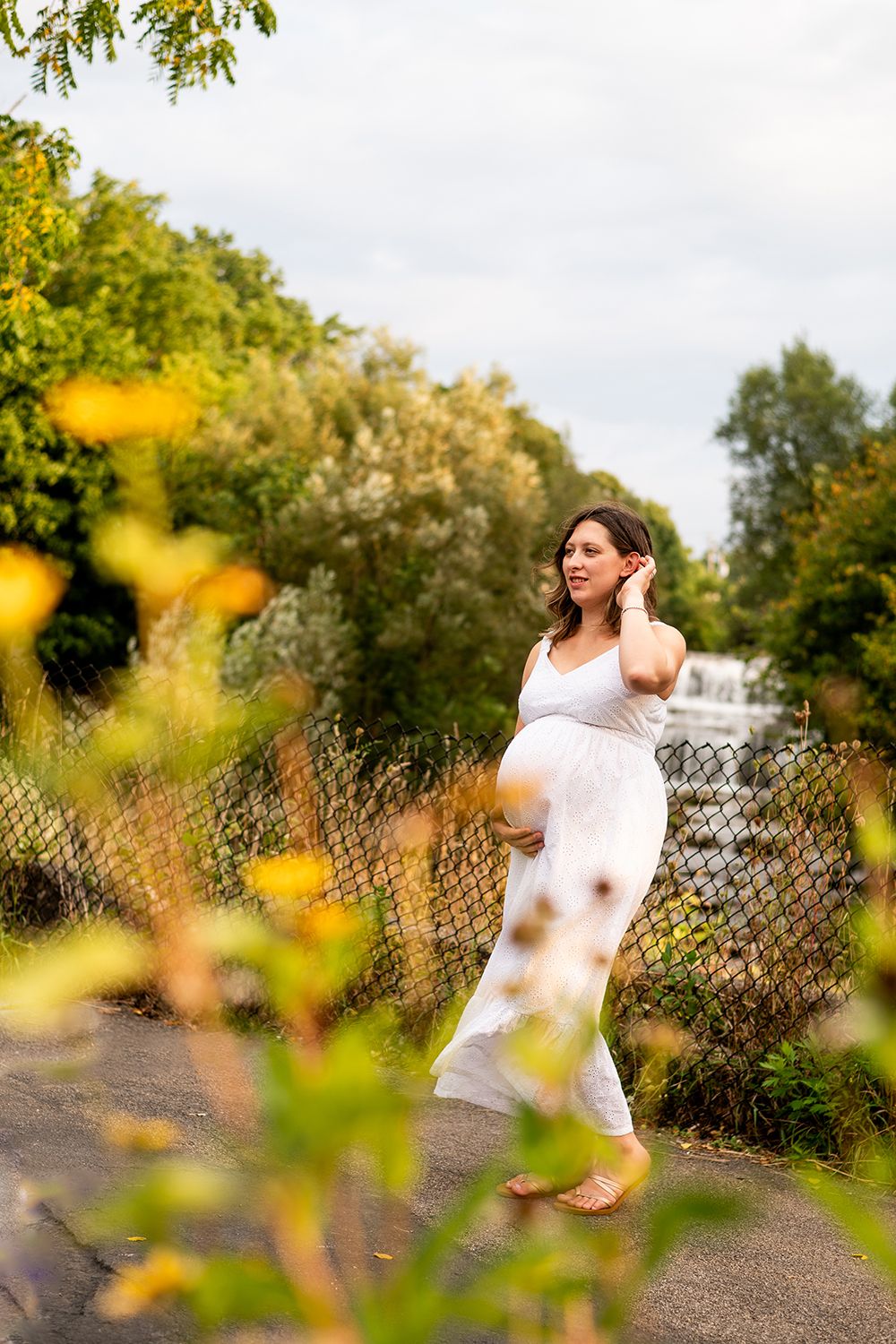 A pregnancy portrait captured in a natural setting with golden flowers and a cascading waterfall in the distance.