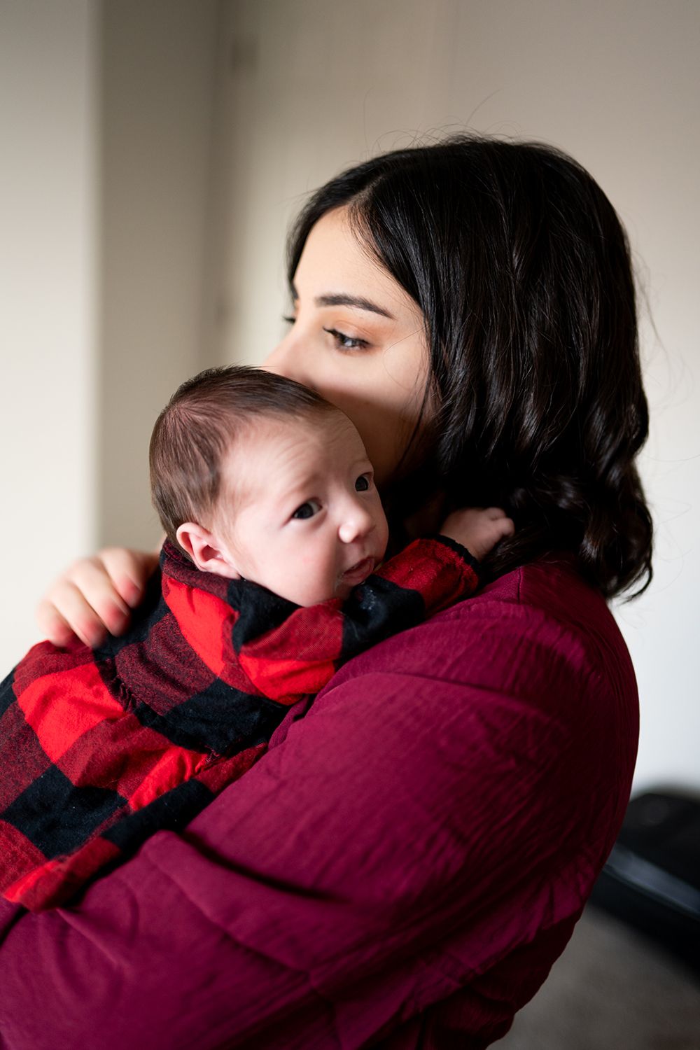 A series of four intimate photos showing a parent in burgundy holding and embracing a child in red winter clothing.