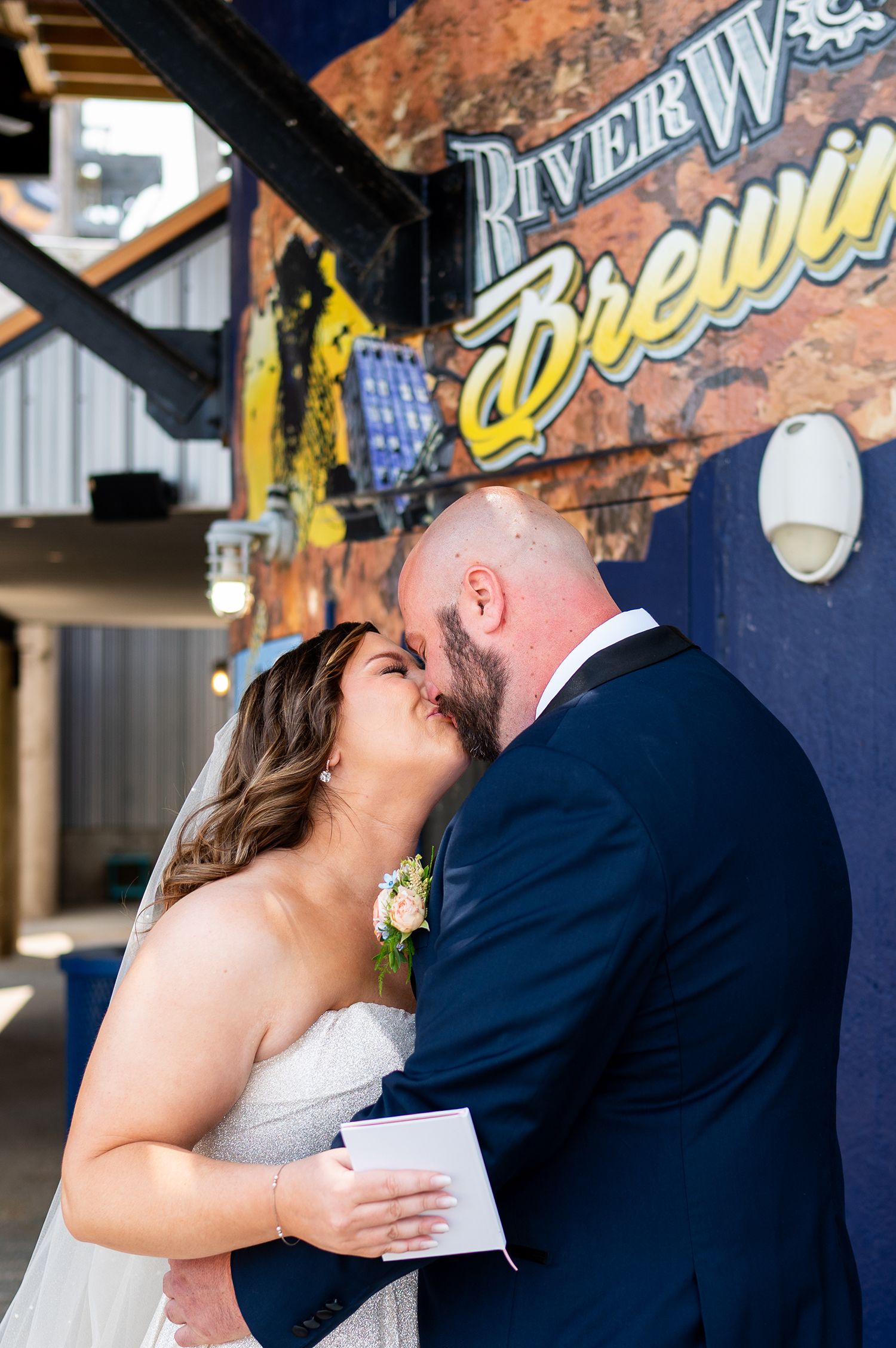 A romantic wedding kiss sequence captured at a brewery venue with rustic decor and signage in the background.