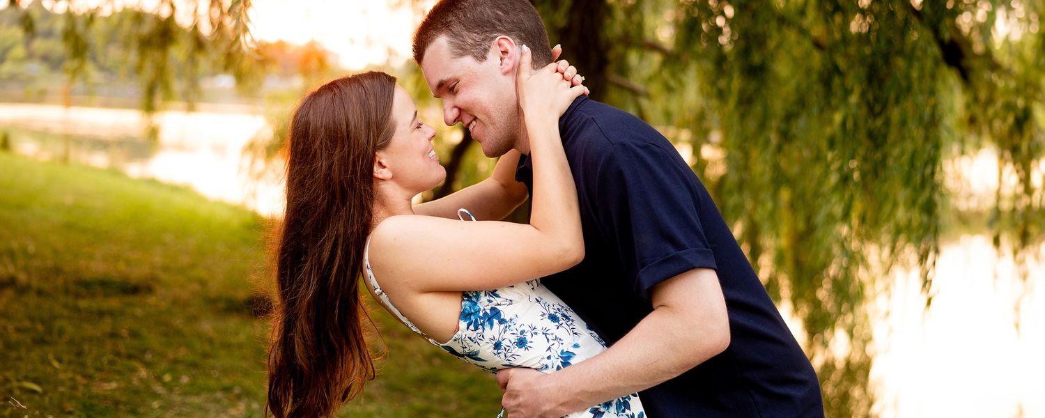 A couple embraces in romantic poses outdoors during golden hour while willow trees frame the background.