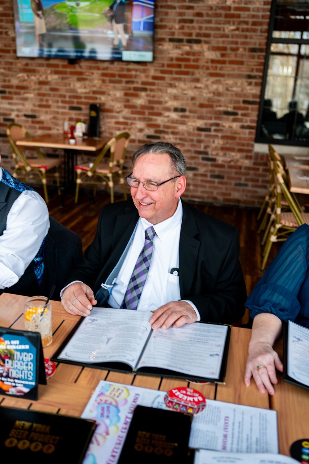 A formal gathering shows a guest reviewing paperwork while seated at a wooden table in a rustic brick venue.