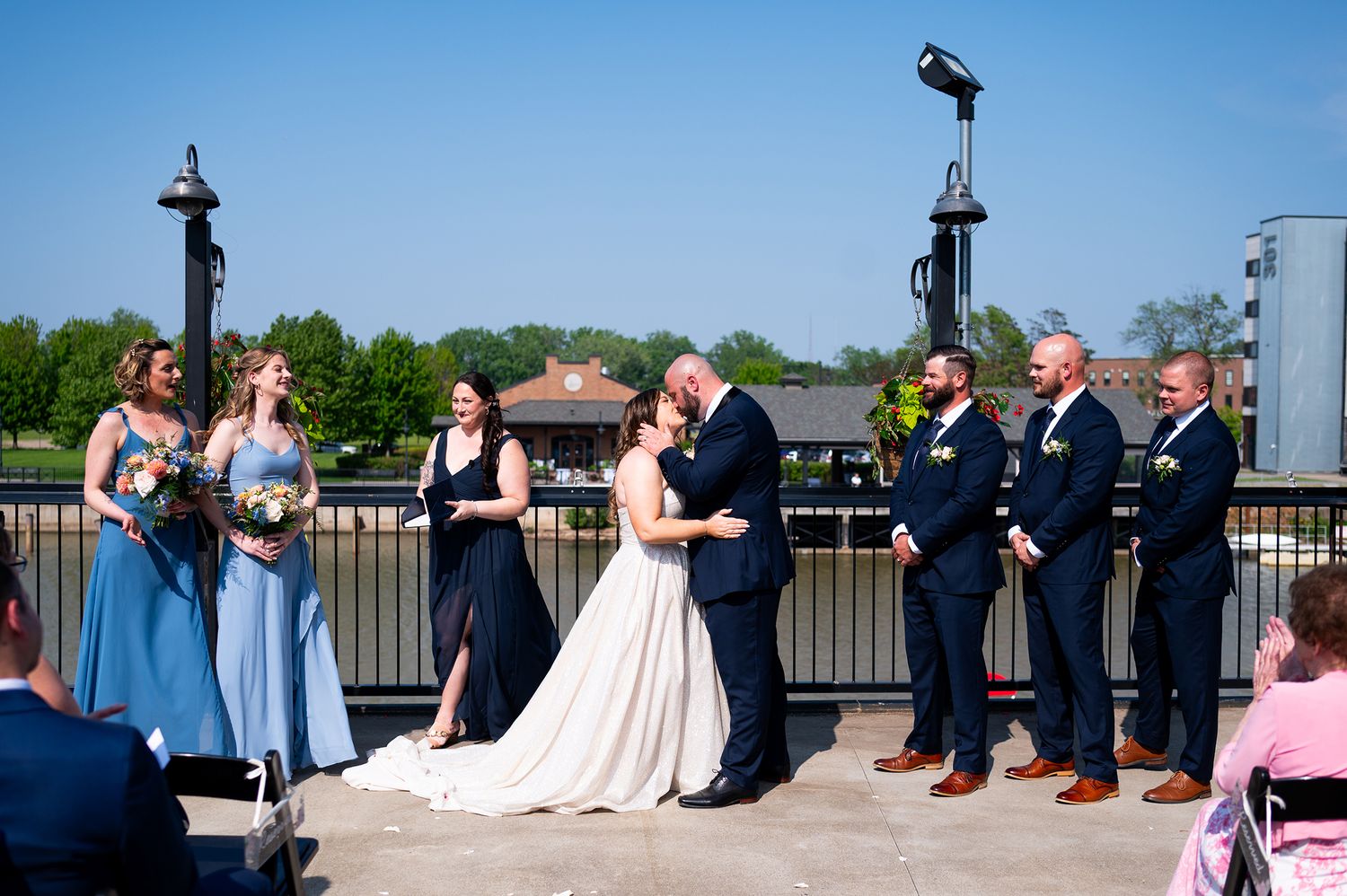 Wedding party poses for photos on a dock overlooking a lake on a sunny summer day.