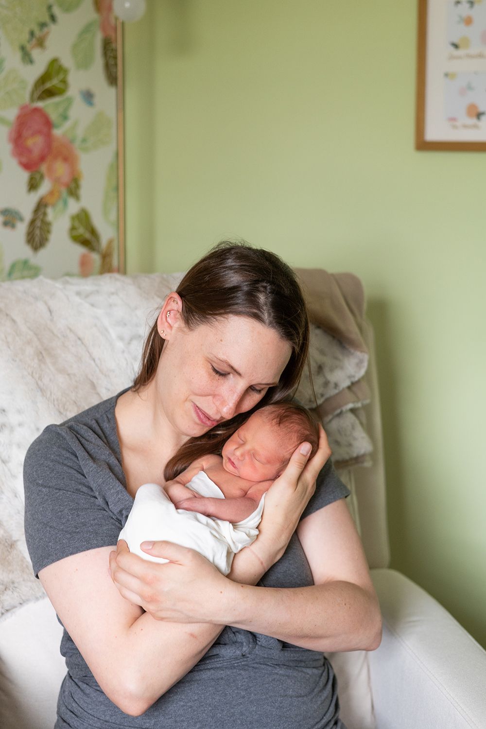 A tender moment between a parent and newborn baby in a softly lit room with floral wallpaper.