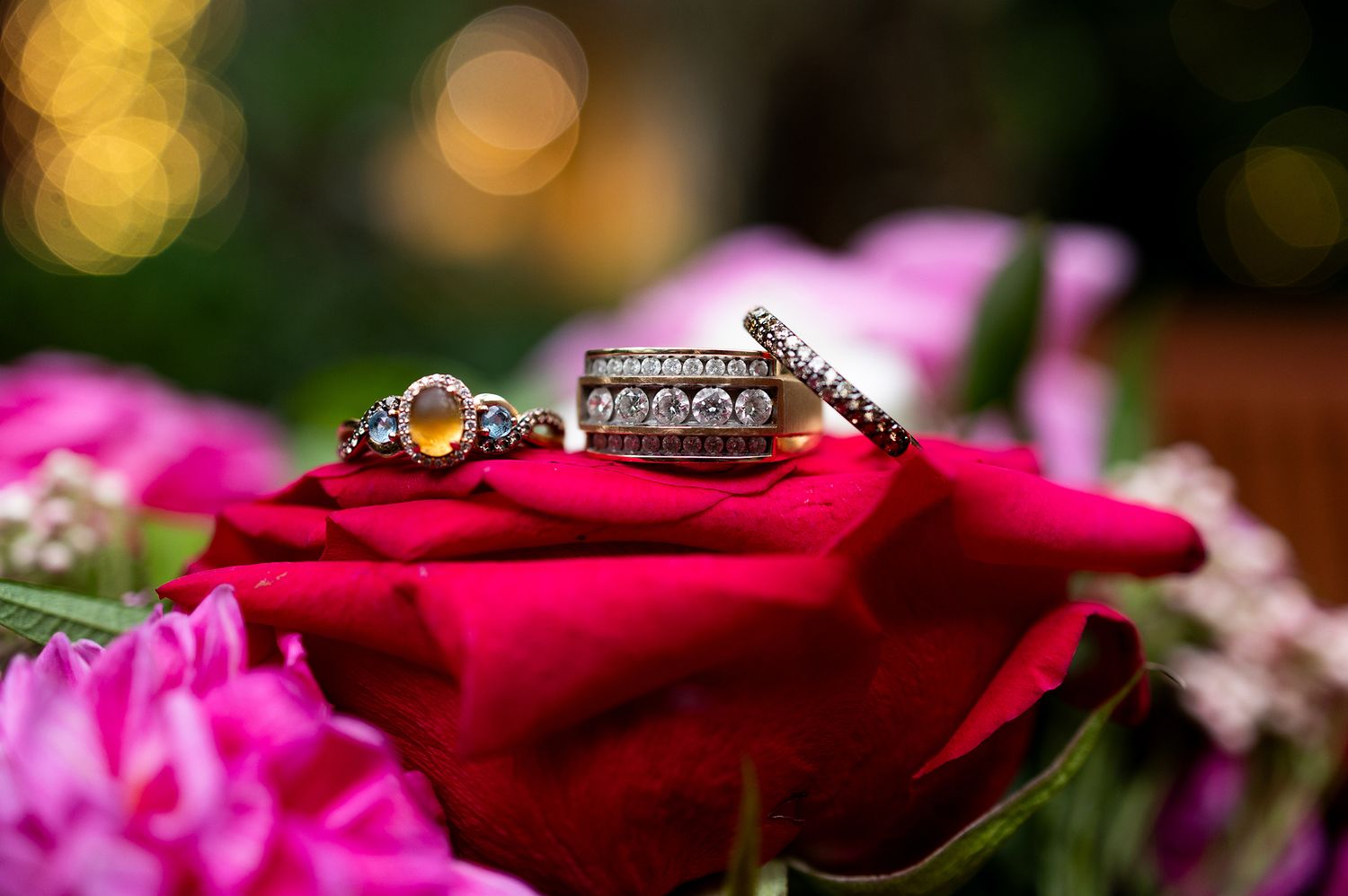 Two diamond rings resting on a vibrant red rose surrounded by pink flowers, perfect for wedding jewelry inspiration.