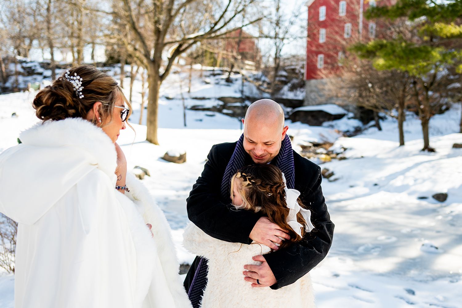 A bride in white and groom in black share a romantic dance moment in the snow with evergreen trees nearby.