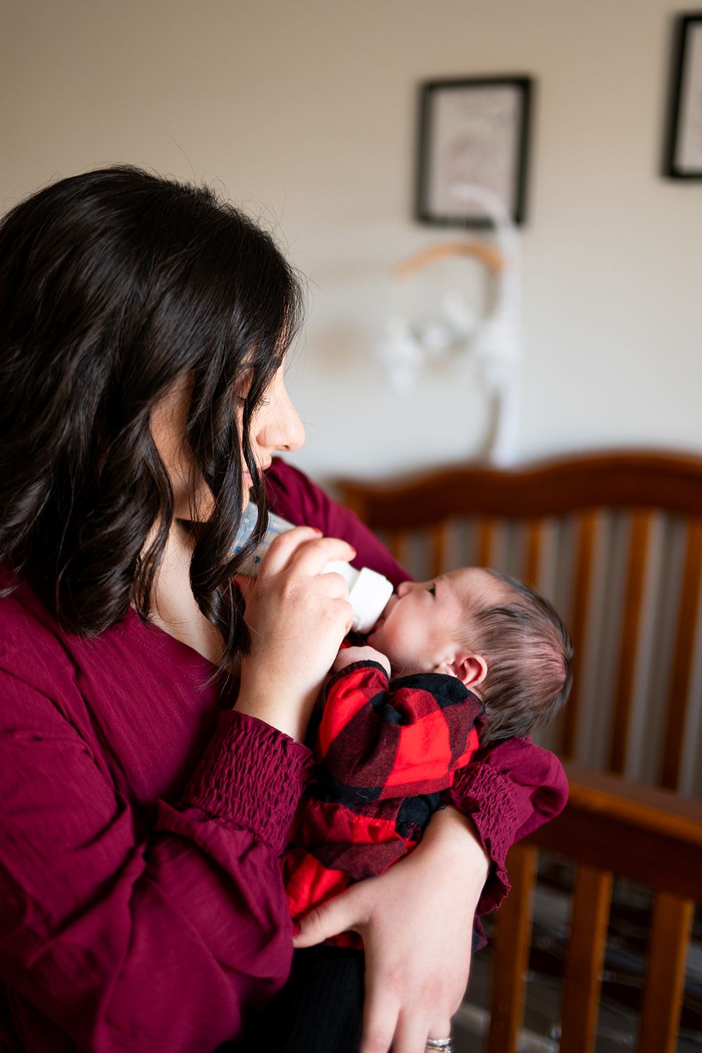 A tender moment of bottle feeding a baby wrapped in burgundy and red clothing in a nursery setting.