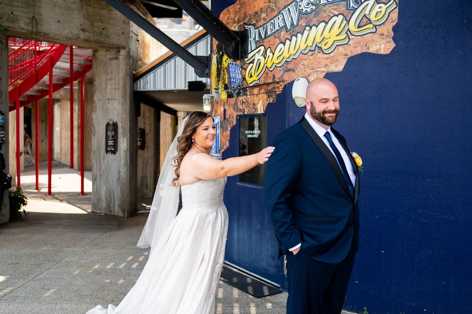 A couple shares a joyful moment together in a rustic brick-walled setting during their wedding celebration.