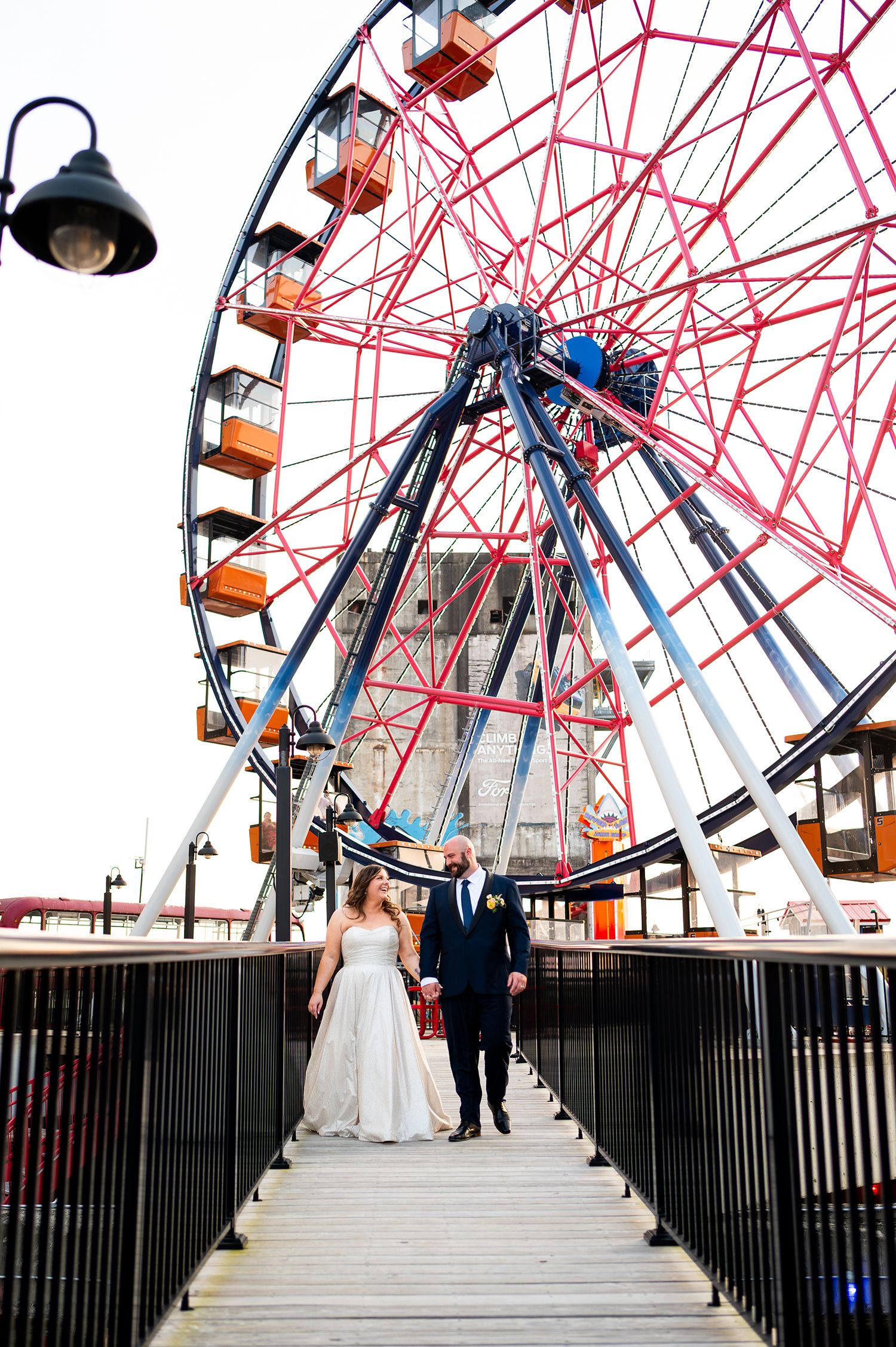 Wedding couple poses in front of a red and white ferris wheel at an amusement park.