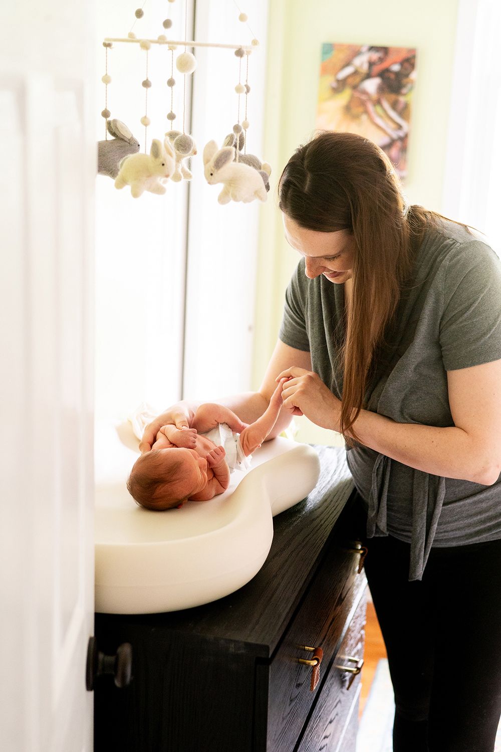 A baby lies on a changing table while being cared for in a softly lit nursery with white curtains and hanging decorations.