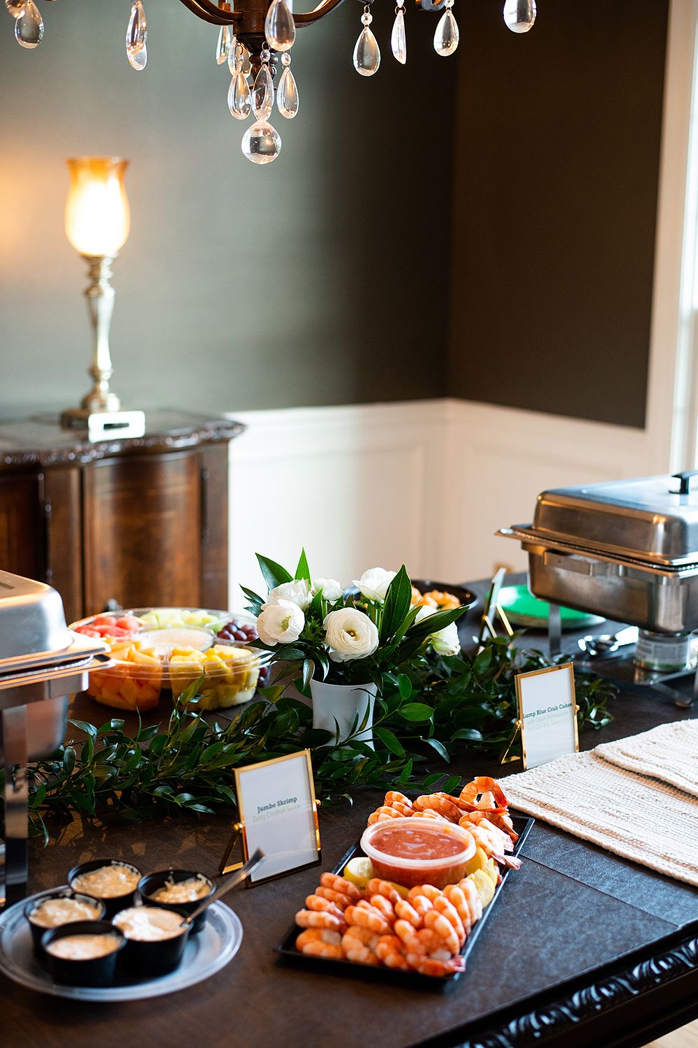 Elegant event setup with string lights overhead and a dark table displaying appetizers and decorative greenery.