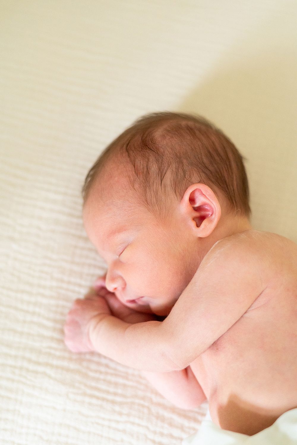 Peaceful sleeping newborn baby laying on soft cream-colored blanket in natural light.
