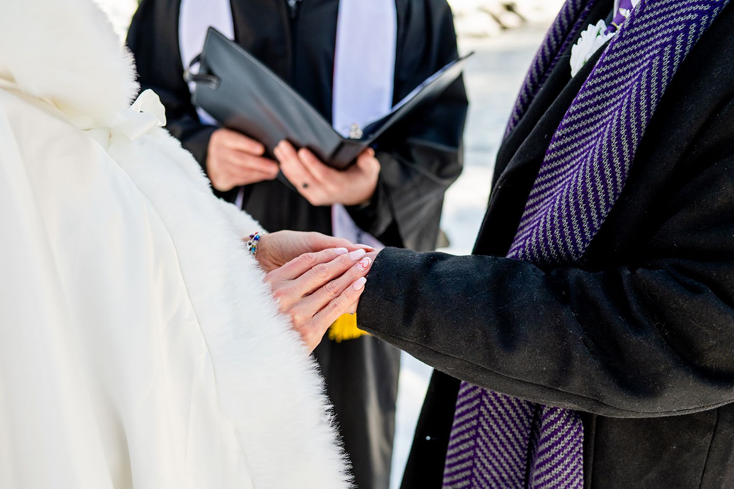 Close-up of wedding ceremony hands exchanging rings with officiant holding book in background.