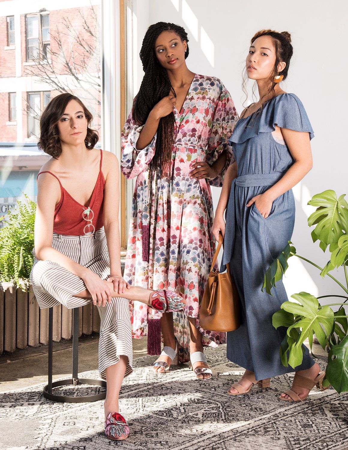 Three women model spring fashion looks including a floral maxi dress, chambray dress, and red camisole with tan pants.