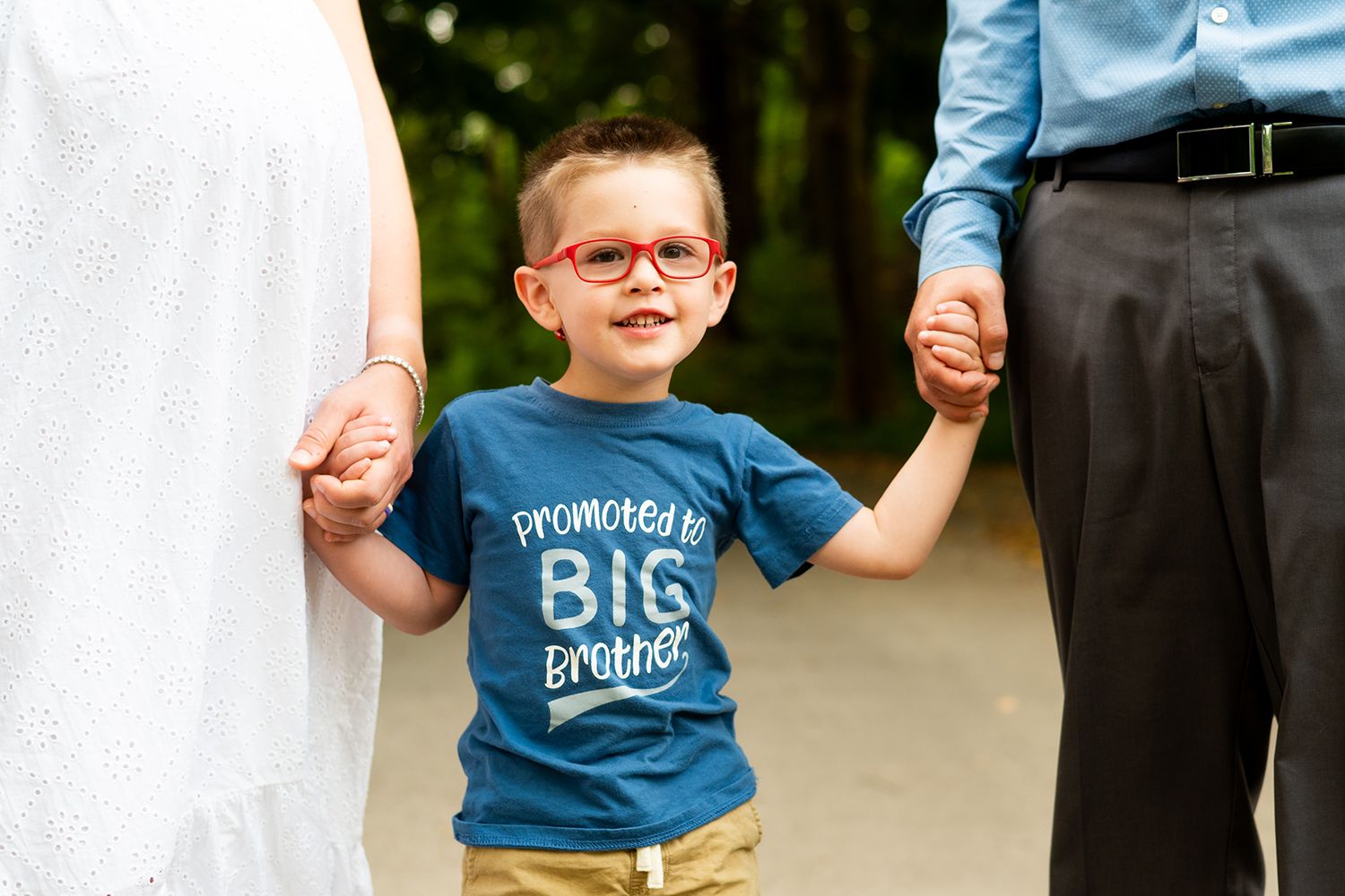 A young child holding hands while wearing a blue t-shirt and khaki pants walks between two people outdoors.