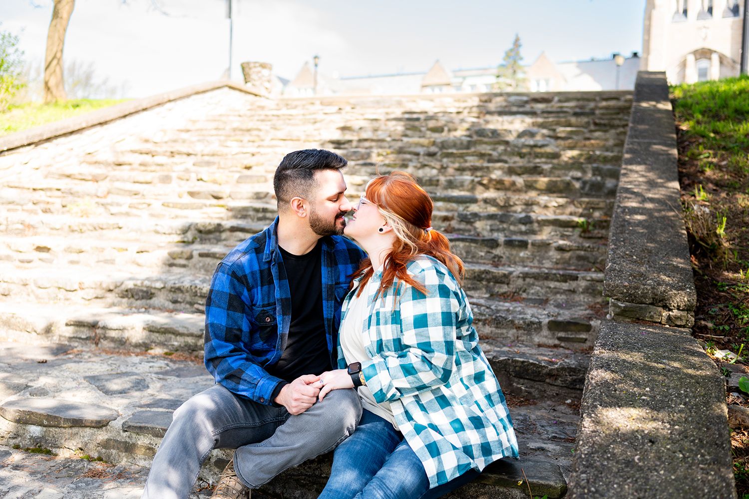 Two people in plaid shirts sit together on stone steps in warm sunlight.