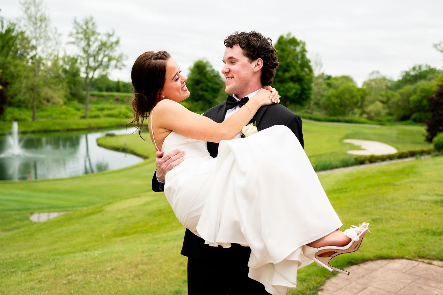 Joyful couple embraces on a lush green golf course with rolling hills and a pond in the background.