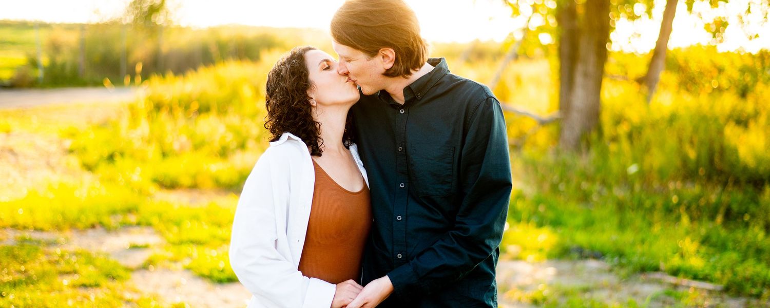 A couple embraces during sunset in a golden-lit field with dreamy outdoor lighting and romantic ambiance.