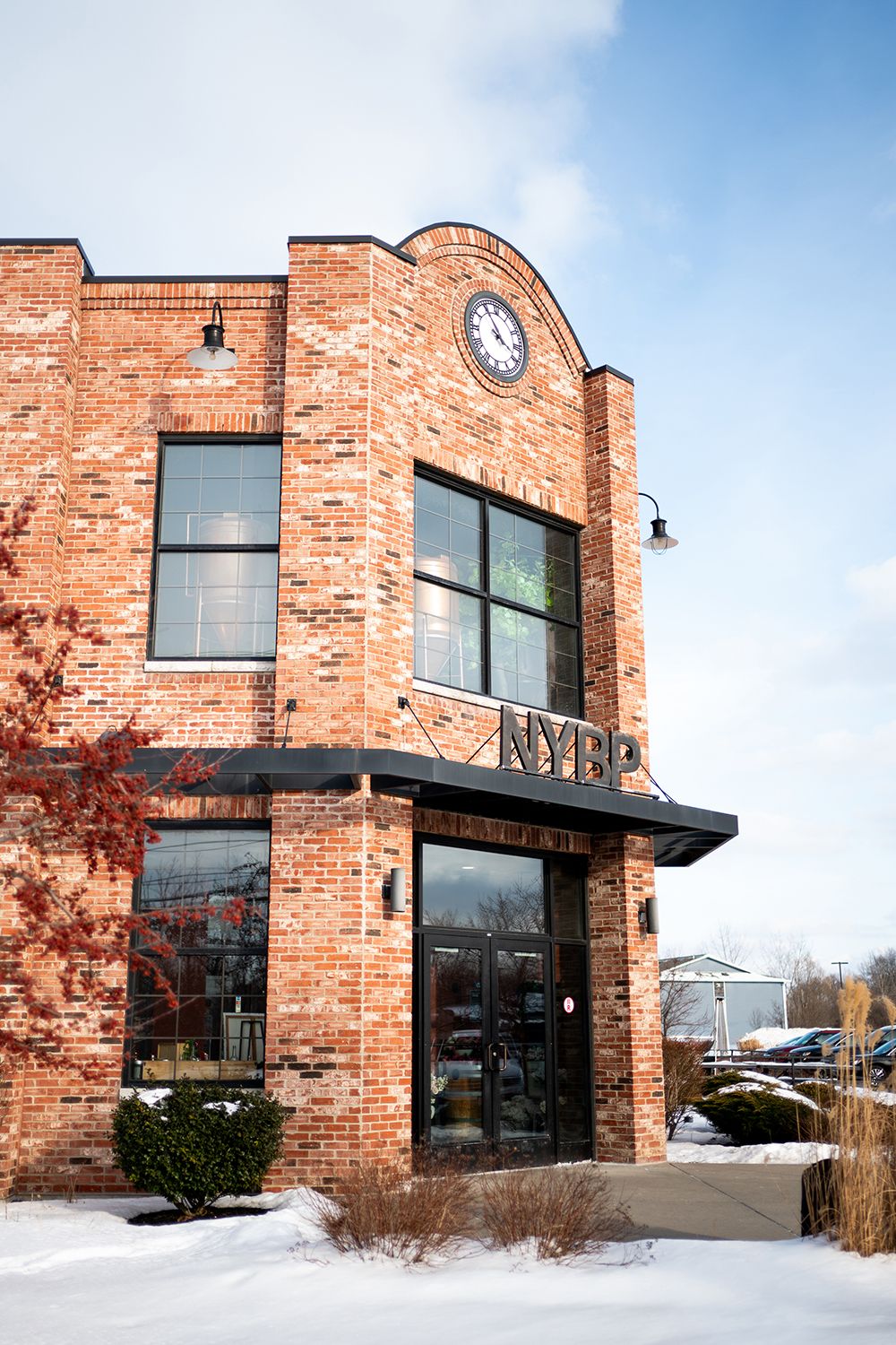 Exterior view of a historic two-story brick building with large windows and a clock feature on a snowy day.