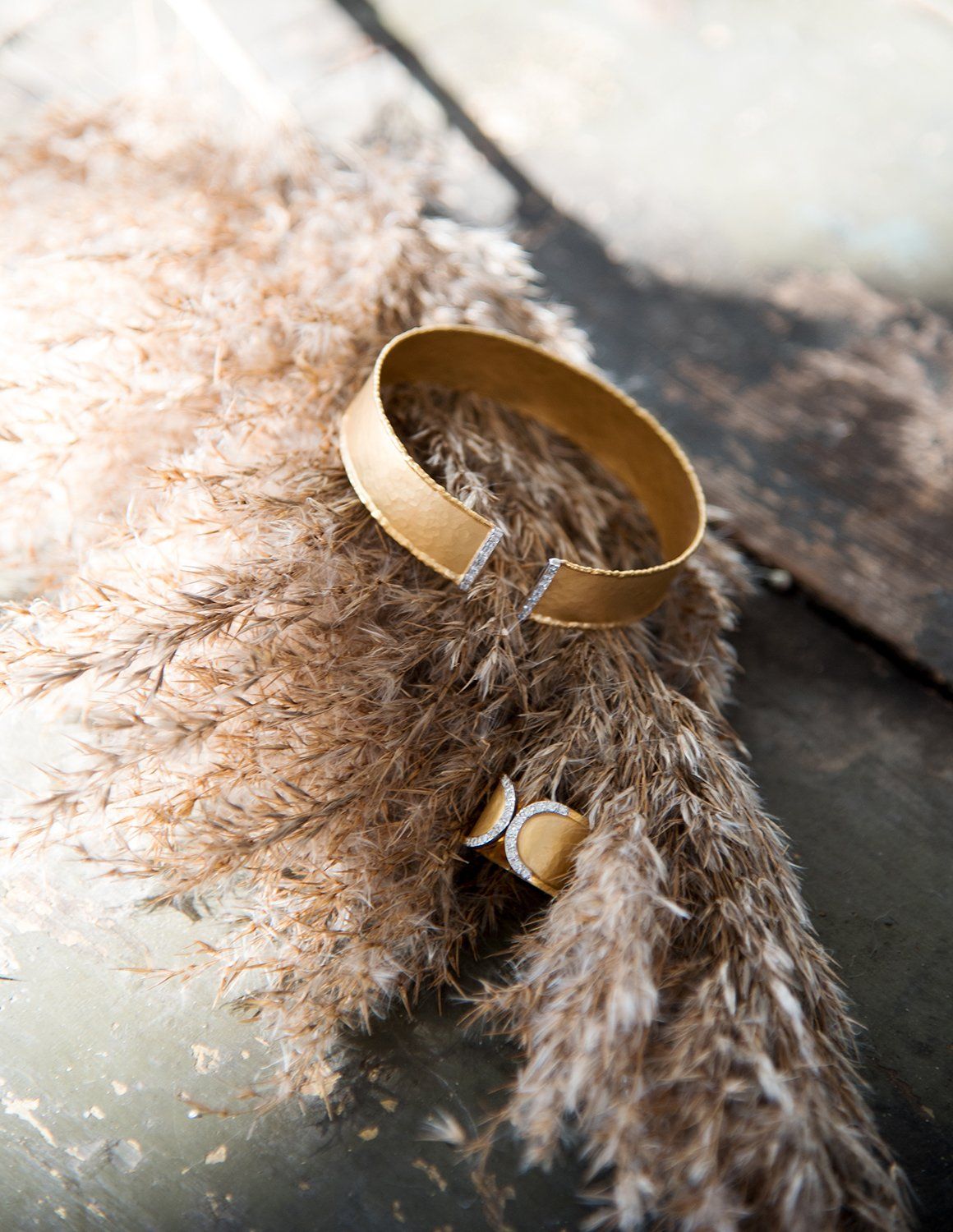 A gold wedding band resting on soft brown pampas grass with delicate wispy texture in natural lighting.